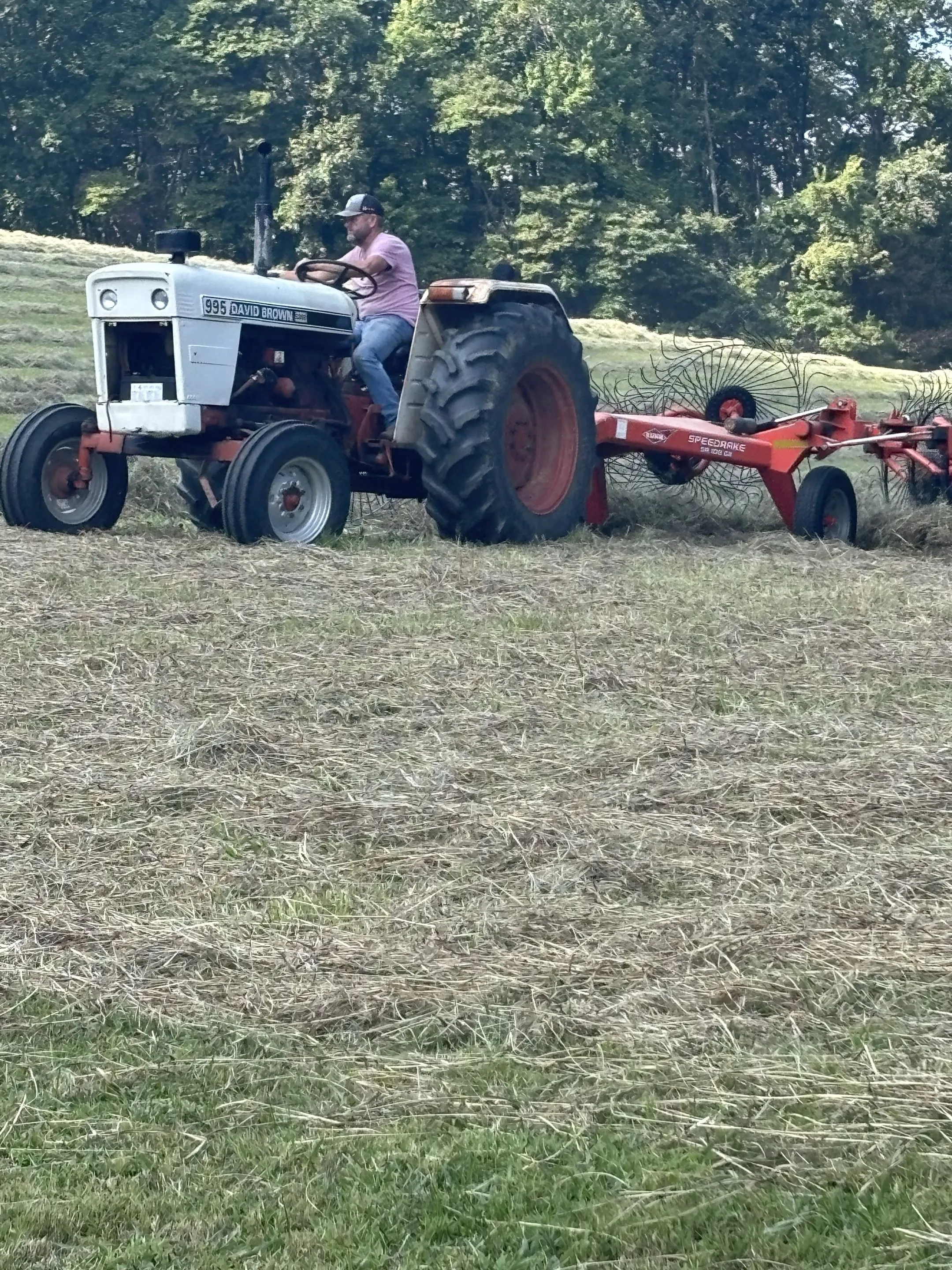 Michael Cavins driving a tractor pulling a hay rake across a freshly cut Claiborne County field