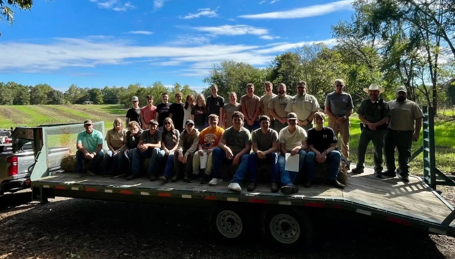 A large group of students, instructors, and TWRA officers gathered on a hay trailer at an outdoor education event