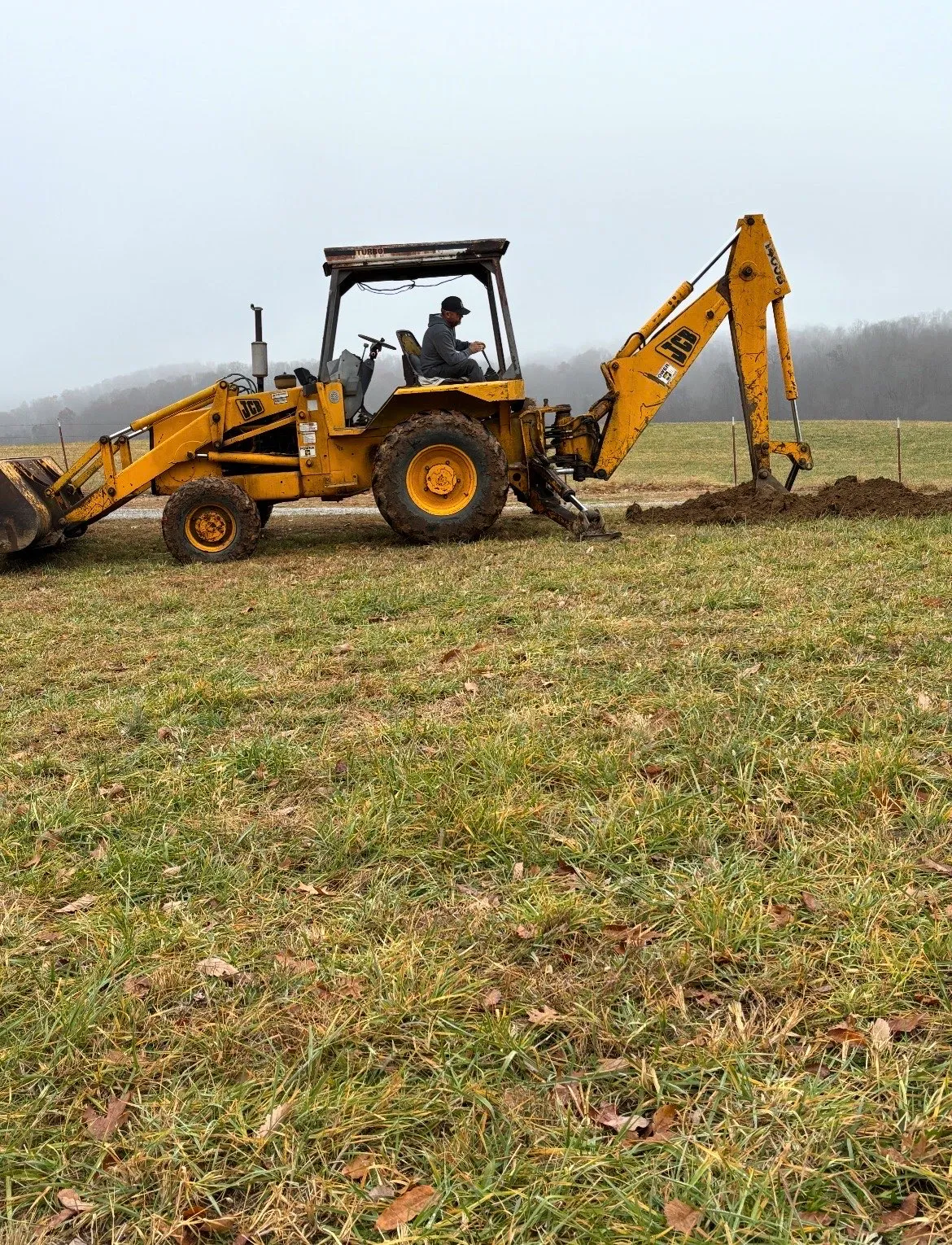 Michael Cavins operating a backhoe in a field on a foggy morning