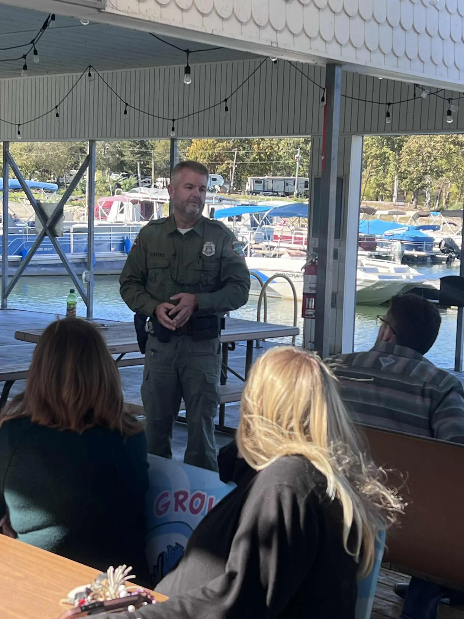 Michael Cavins in his TWRA Game Warden uniform speaking with residents at a lakeside marina pavilion