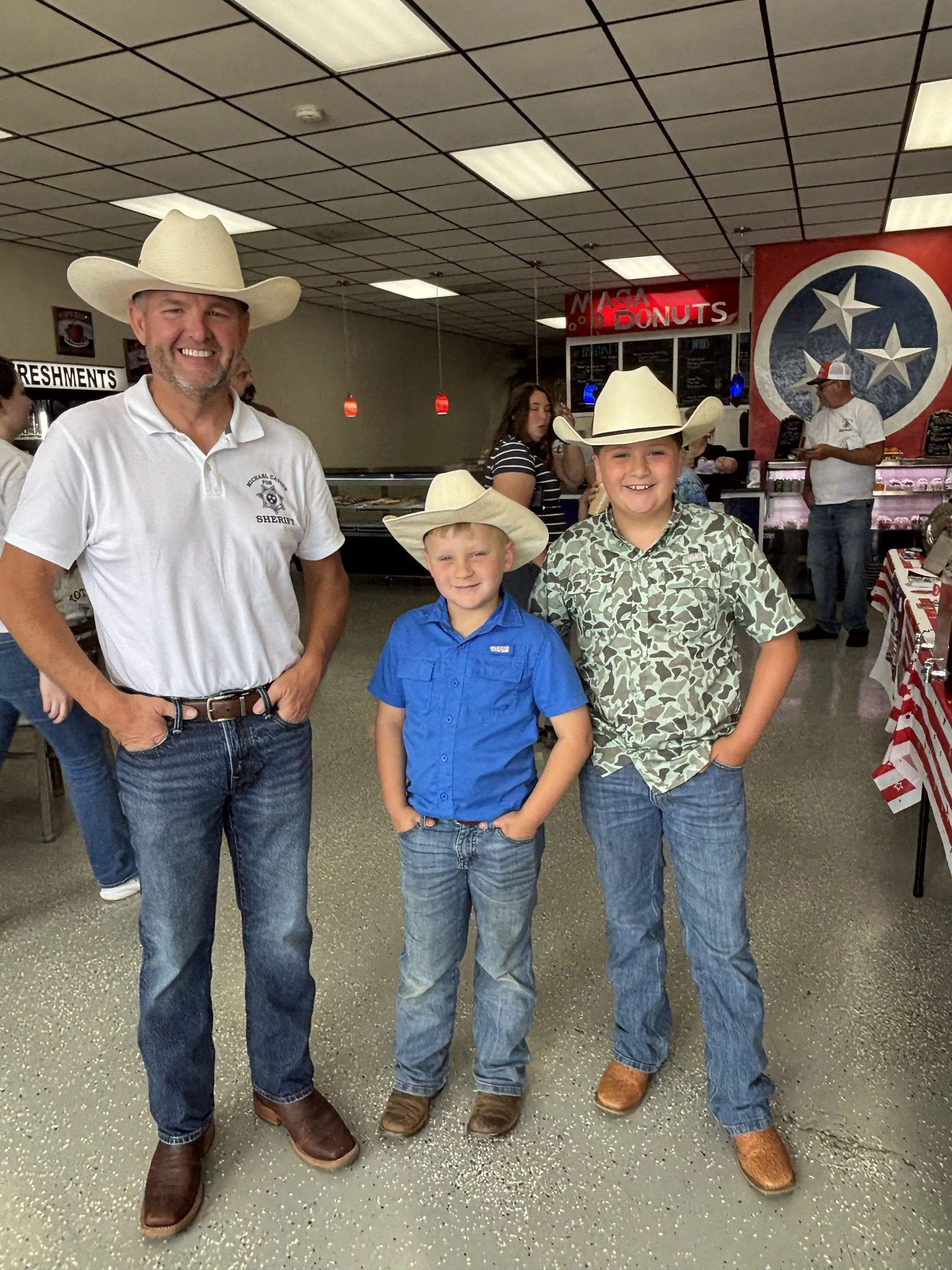 Michael Cavins with two young supporters in cowboy hats at the MAGA Donuts meet and greet