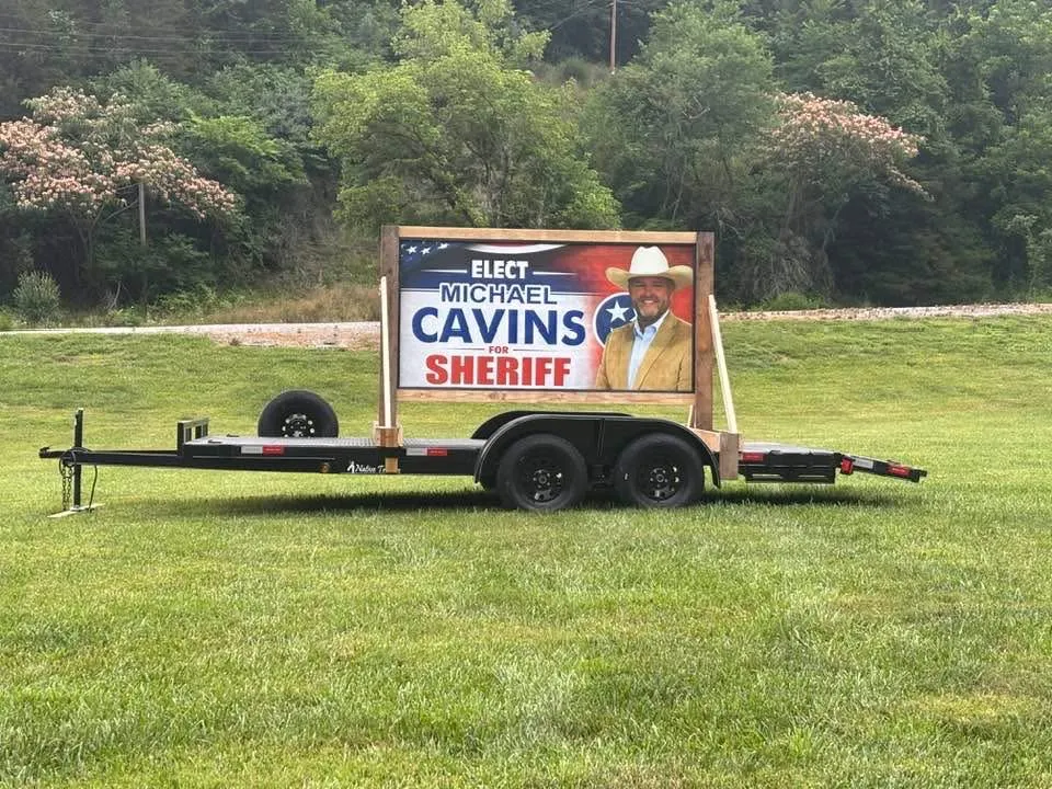 An Elect Michael Cavins for Sheriff sign mounted on a trailer parked on a grassy field